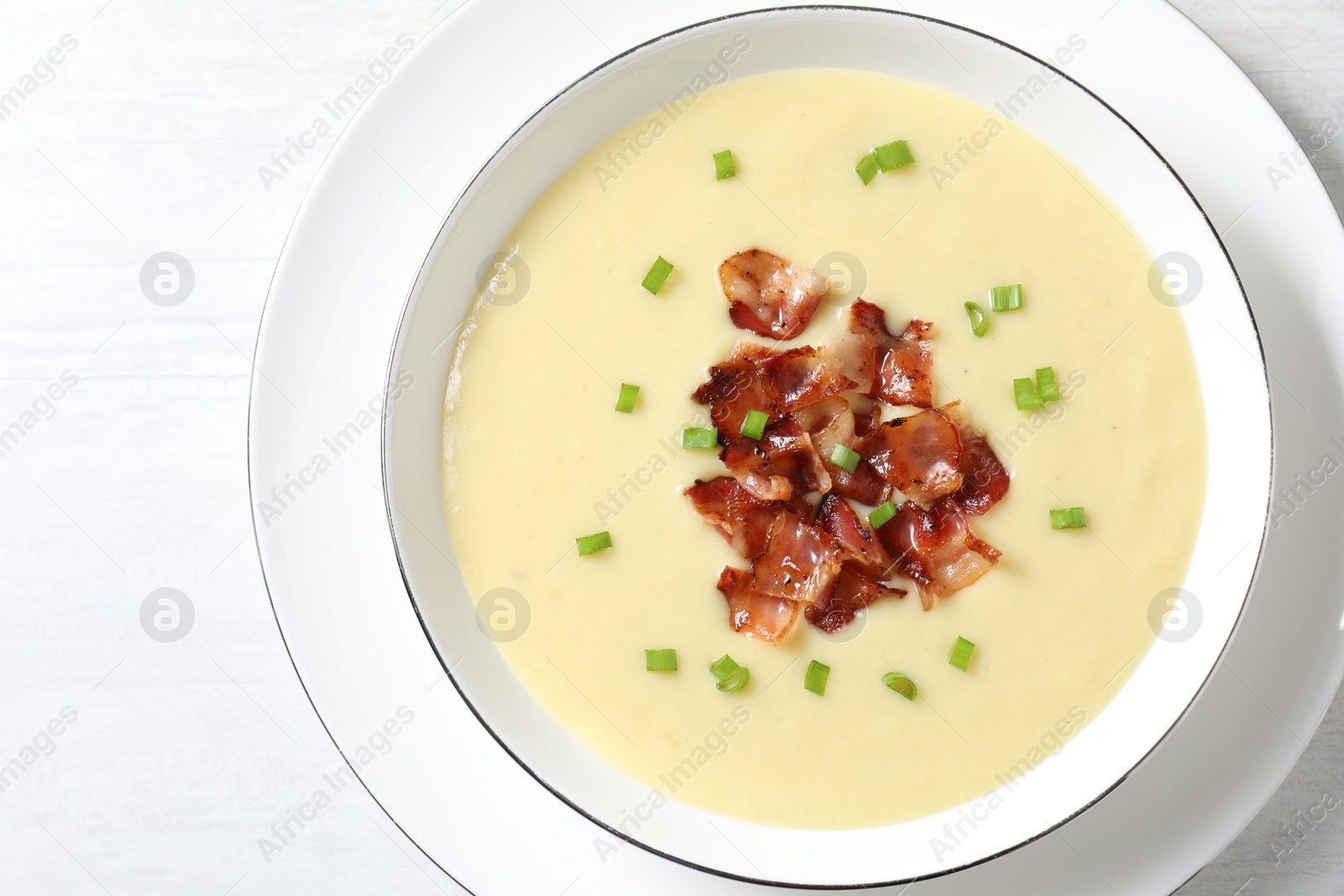 Photo of Tasty potato soup with bacon and green onion in bowl on white table, top view