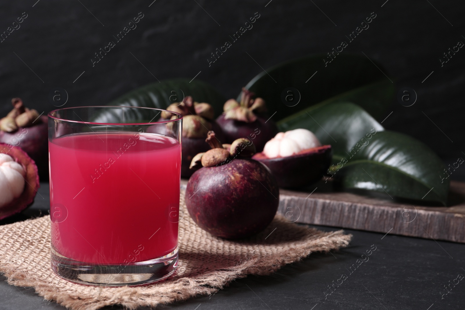 Photo of Delicious fresh mangosteen juice in glass on dark table, space for text