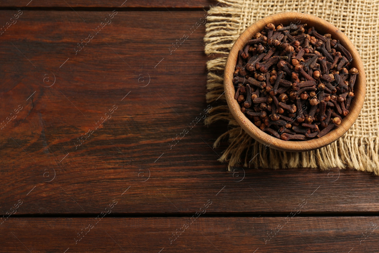 Photo of Aromatic dry cloves in bowl on wooden table, top view. Space for text