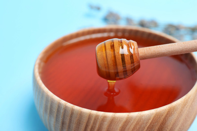 Photo of Wooden bowl with organic honey and dipper on light blue background, closeup