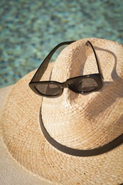 Stylish hat and sunglasses near outdoor swimming pool on sunny day