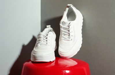 Photo of Pair of stylish sneakers on ottoman near grey wall