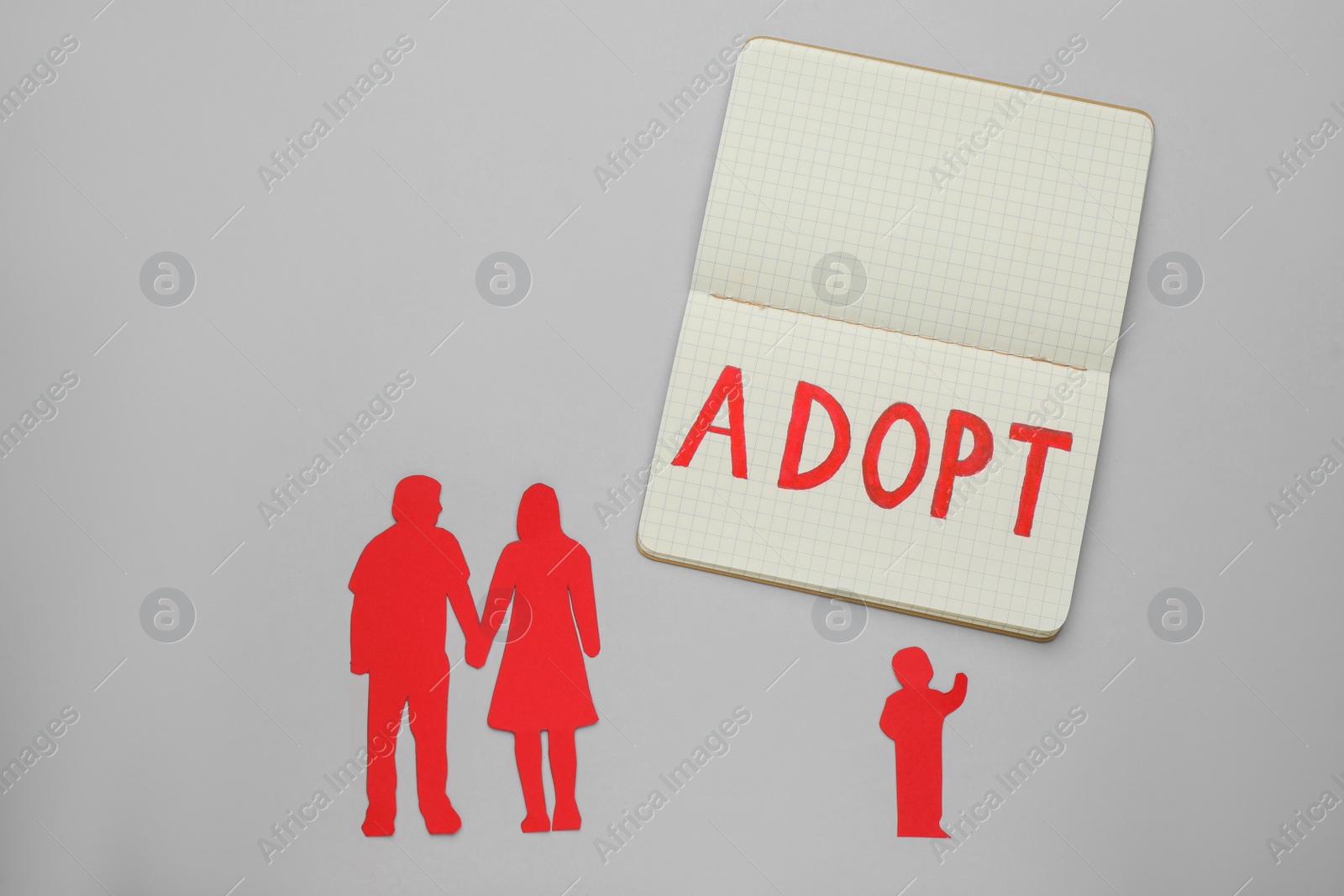 Photo of Figures of parents with child and word Adopt in notebook on grey background, flat lay