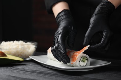 Chef in gloves making sushi rolls with shrimps at black wooden table, closeup