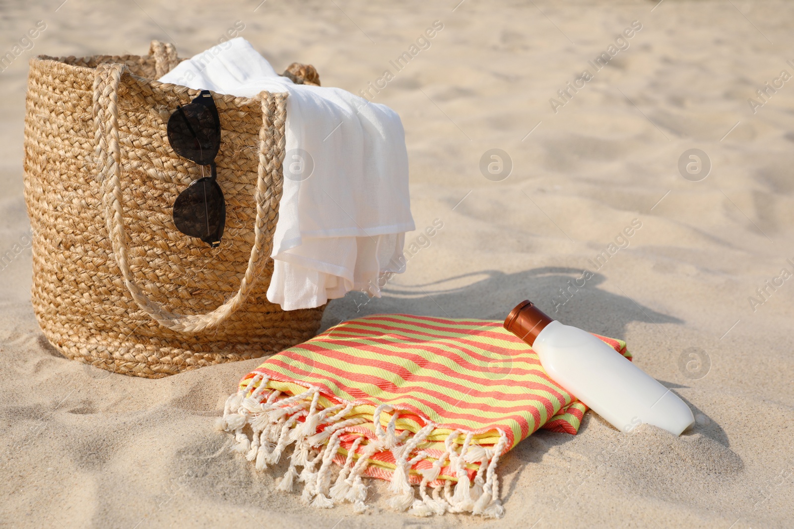 Photo of Beach bag, towel, blanket, sunglasses and sunscreen on sand