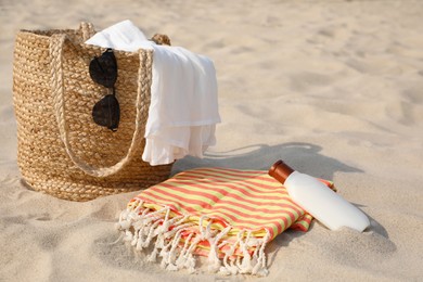 Photo of Beach bag, towel, blanket, sunglasses and sunscreen on sand