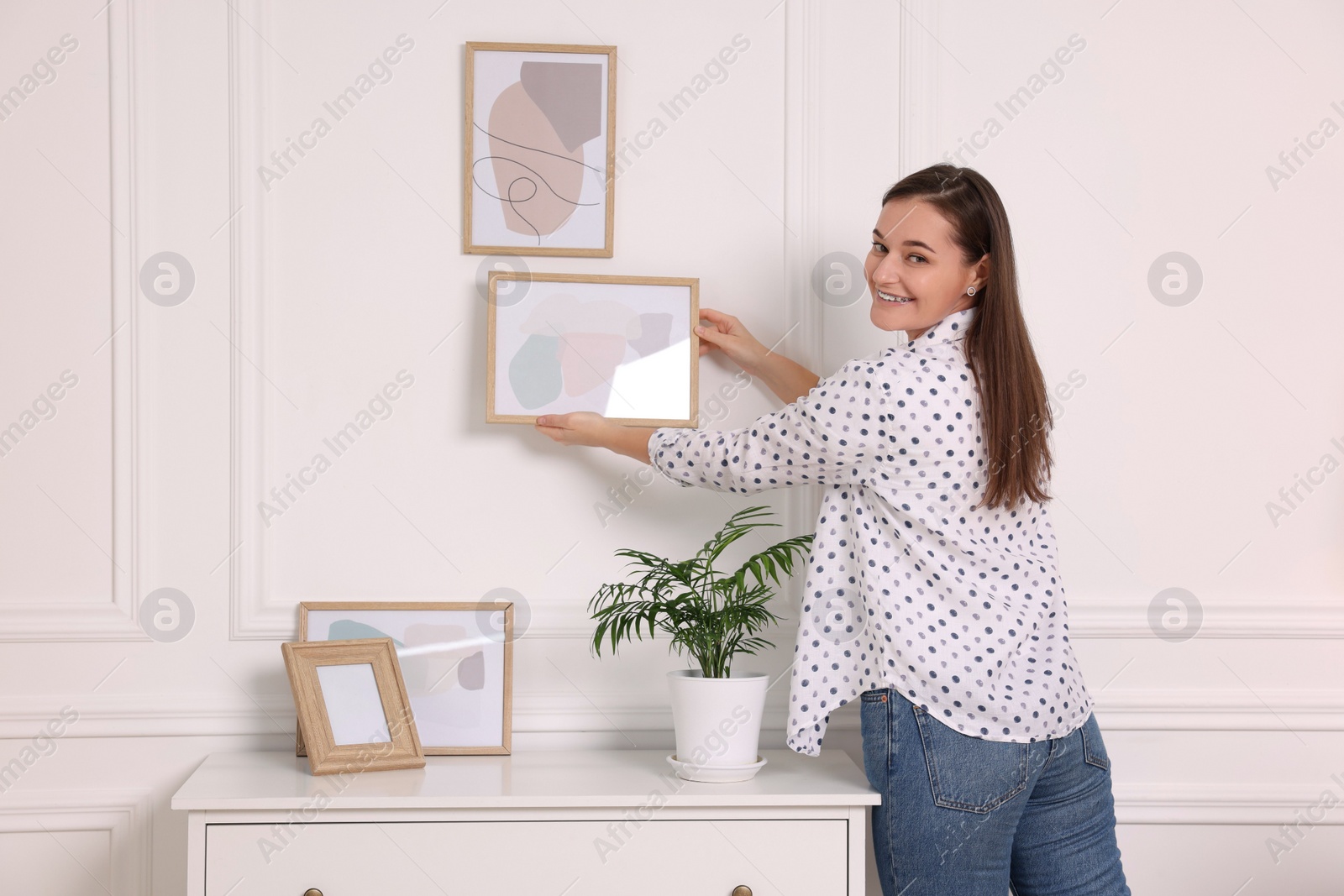 Photo of Woman hanging picture frame on white wall at home