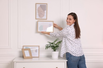 Woman hanging picture frame on white wall at home