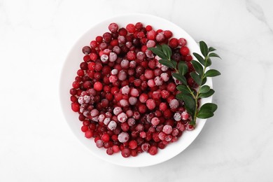 Frozen red cranberries and green leaves on white marble table, top view