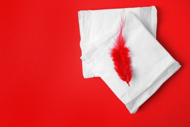 Photo of Packed menstrual pads and red feather on color background, flat lay with space for text. Gynecological care