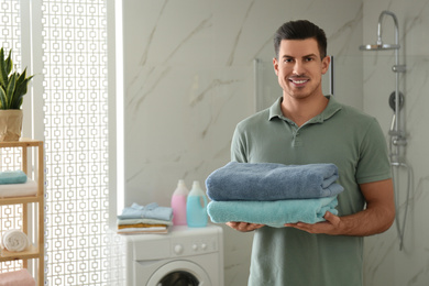 Photo of Happy man with clean towels in bathroom. Laundry day