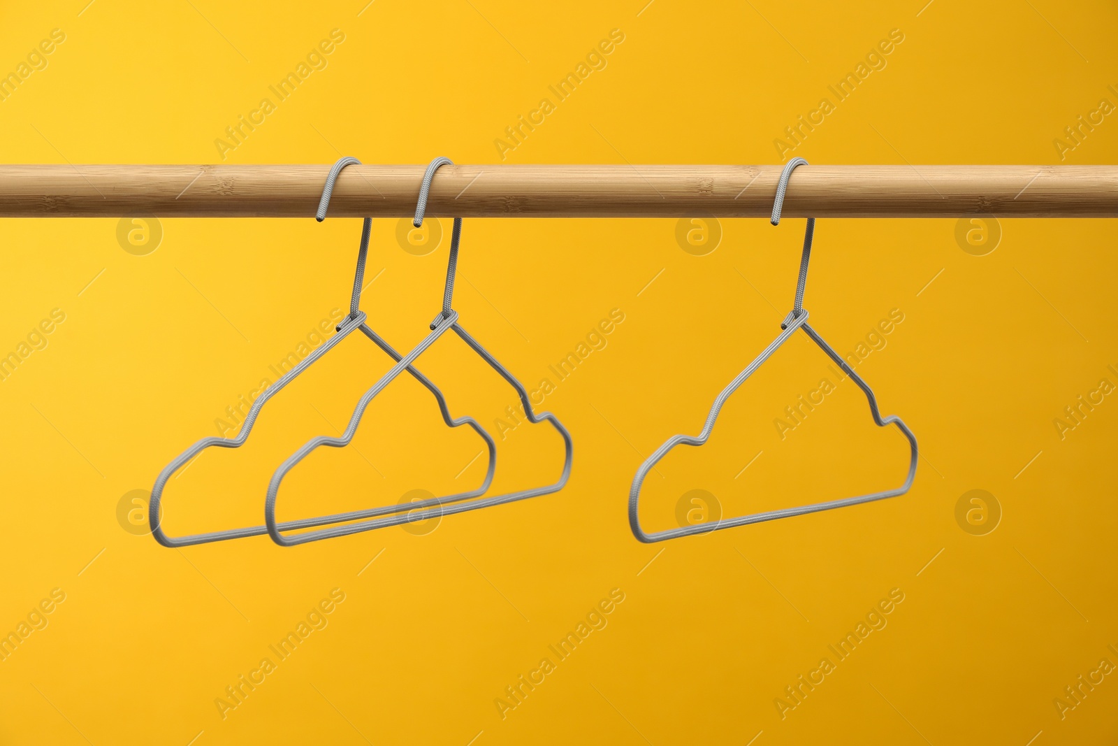 Photo of Empty clothes hangers on wooden rack against orange background