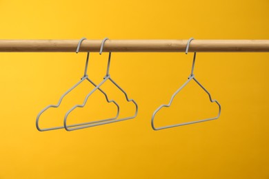 Photo of Empty clothes hangers on wooden rack against orange background