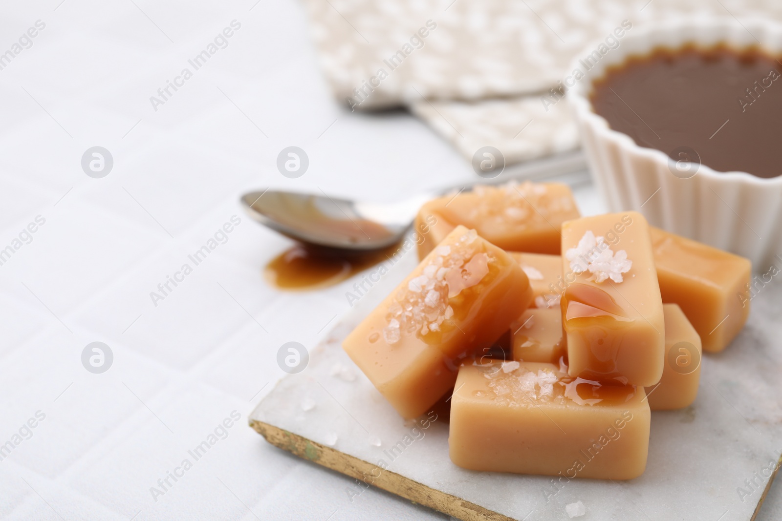 Photo of Delicious candies with sea salt and caramel sauce on white tiled table, closeup