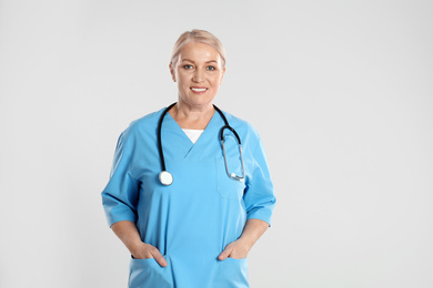 Portrait of mature doctor with stethoscope on light grey background