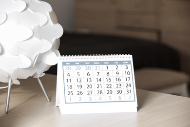 Paper calendar and decorative lamp on wooden table indoors