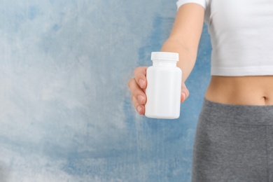 Photo of Slim woman holding bottle of weight loss pills against color background, closeup. Space for text