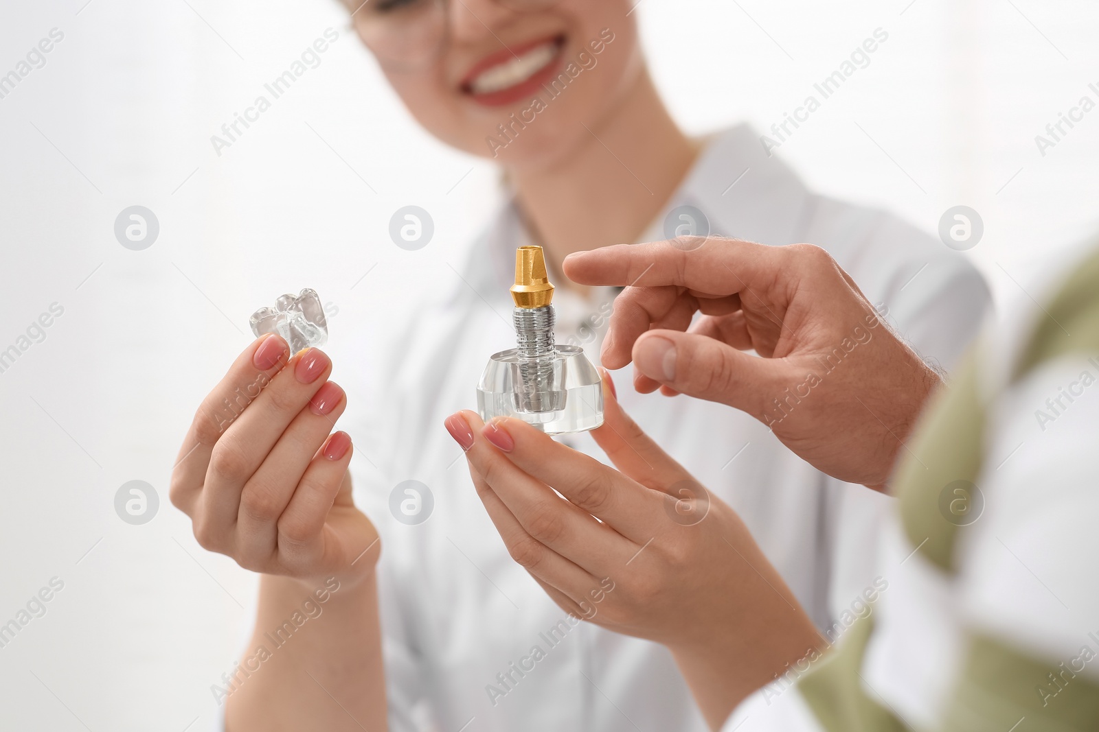 Photo of Doctor with educational model of dental implant consulting patient in clinic, closeup