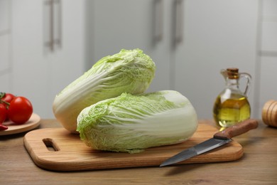 Photo of Fresh Chinese cabbages, knife, tomatoes and oil on wooden table in kitchen