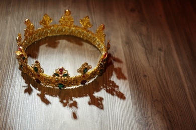 Photo of Beautiful golden crown with gems on wooden table. Fantasy item