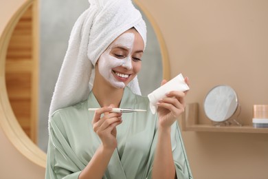 Photo of Woman applying face mask onto brush in bathroom. Spa treatments