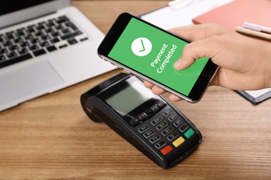 Woman using terminal for contactless payment with smartphone at wooden table, closeup. Transaction completed screen on device