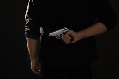 Professional killer with gun on black background, closeup