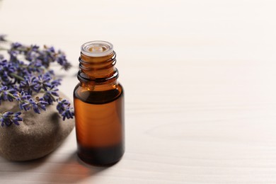 Photo of Bottle of essential oil and lavender flowers on white wooden table, space for text