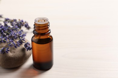 Bottle of essential oil and lavender flowers on white wooden table, space for text