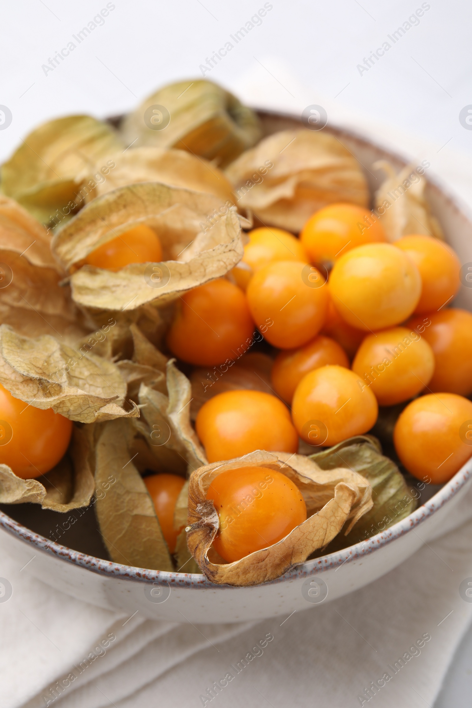 Photo of Ripe physalis fruits with calyxes in bowl on white table, closeup