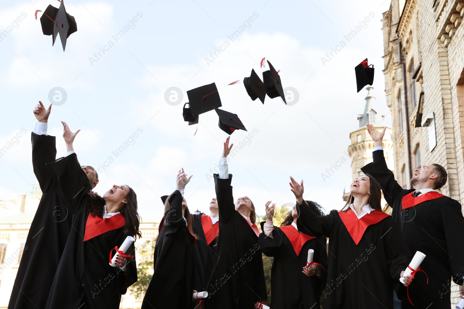 Photo of Happy students with diplomas throwing graduation hats in air outdoors