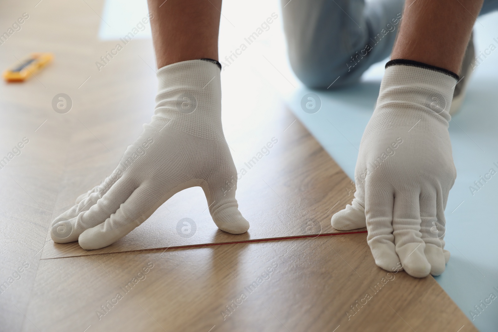 Photo of Worker installing laminated wooden floor indoors, closeup