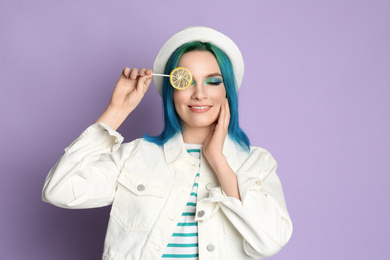 Photo of Young woman with bright dyed hair holding candy on lilac background