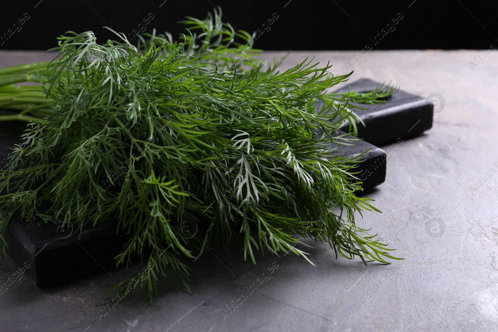 Photo of Board with sprigs of fresh dill on grey textured table against black background, closeup