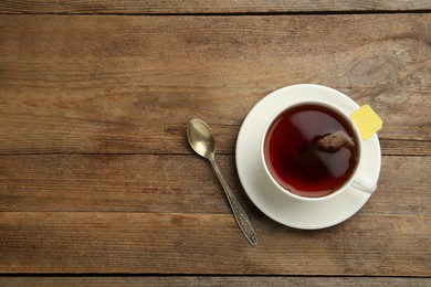 Tea bag in cup of hot water on wooden table, flat lay. Space for text