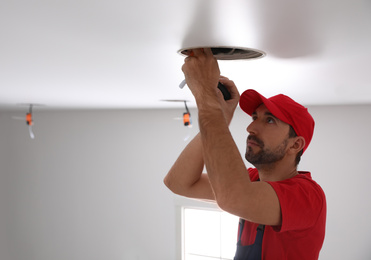 Photo of Worker installing lamp on stretch ceiling indoors