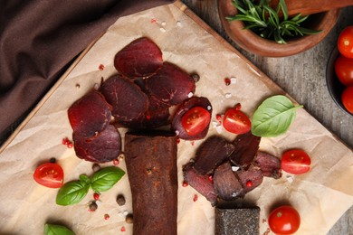 Delicious dry-cured beef basturma with basil, tomatoes and spices on wooden table, flat lay