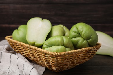 Photo of Cut and whole chayote in wicker basket on wooden table, closeup