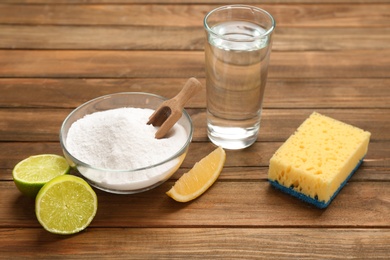 Composition with bowl of baking soda and glass of vinegar on wooden table