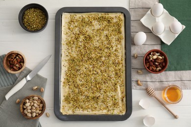 Making delicious baklava. Baking pan with dough and ingredients on white wooden table, flat lay