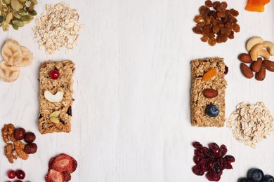 Tasty granola bars and ingredients on white wooden table, flat lay. Space for text