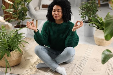 Photo of Relaxing atmosphere. Woman meditating near potted houseplants in room