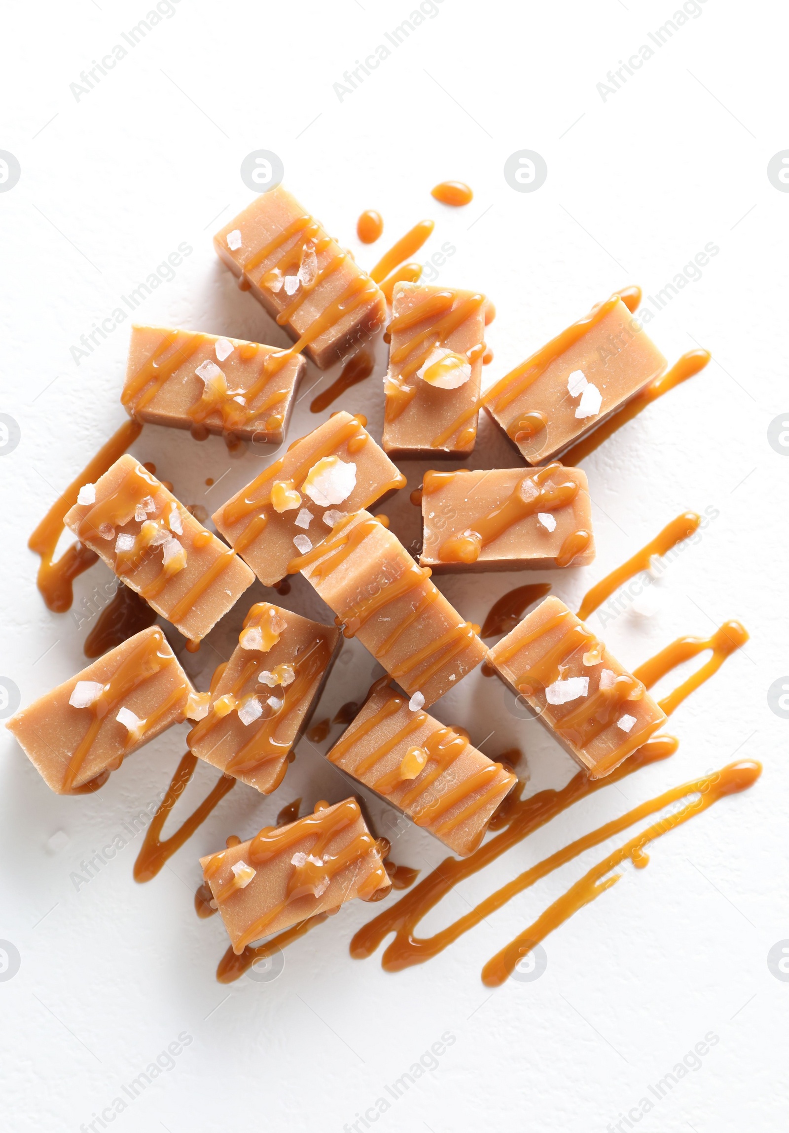 Photo of Tasty candies, caramel sauce and salt on white table, top view