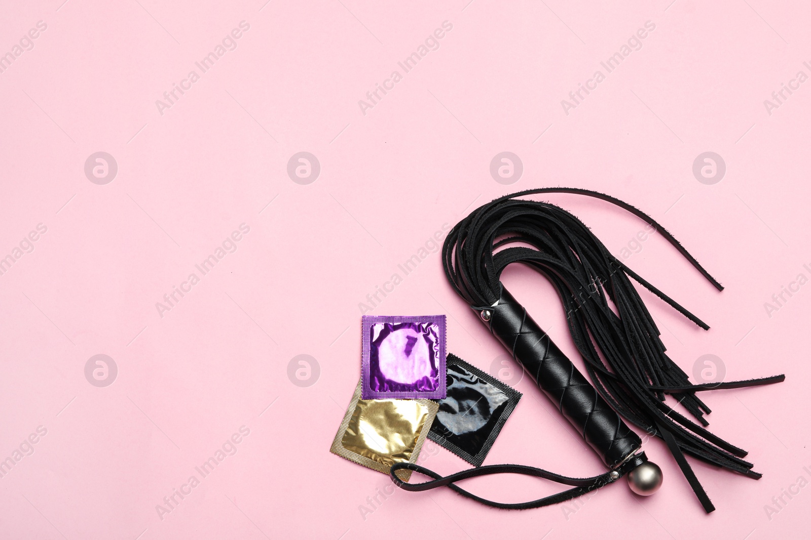 Photo of Whip and condoms on pink background, top view with space for text. Sex game