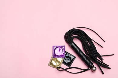 Photo of Whip and condoms on pink background, top view with space for text. Sex game