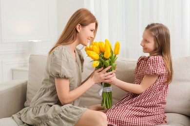 Photo of Daughter congratulating mom with bouquet of yellow tulips at home
