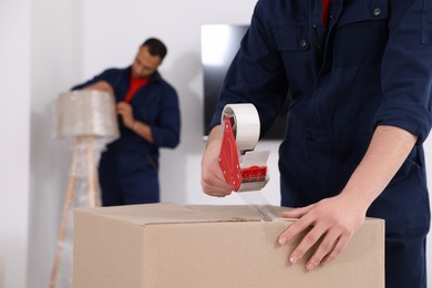 Photo of Male mover packing box with adhesive tape in house, closeup. Space for text