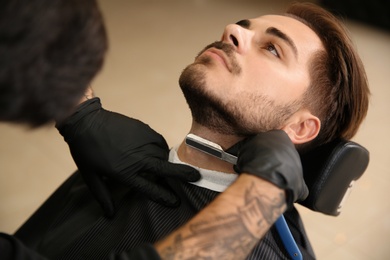 Professional hairdresser shaving client with straight razor in barbershop