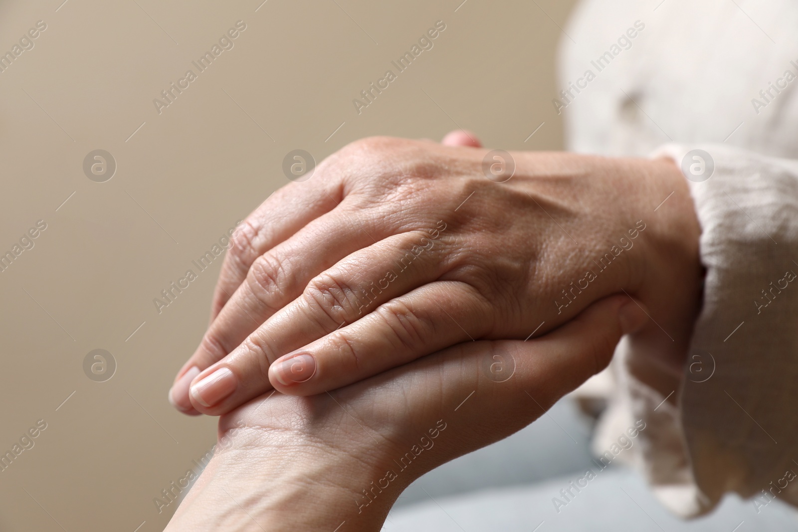 Photo of Woman holding hands with her mother on beige background, closeup