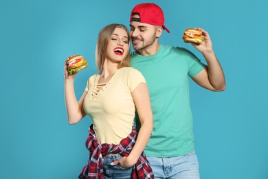 Happy couple with tasty burgers on color background